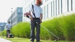 Mitarbeiter des Gebäudeservices Clean Excellence Facility Management mit Helm und Schutzkleidung bei der Grünrasen-Pflege mit Werkzeug.