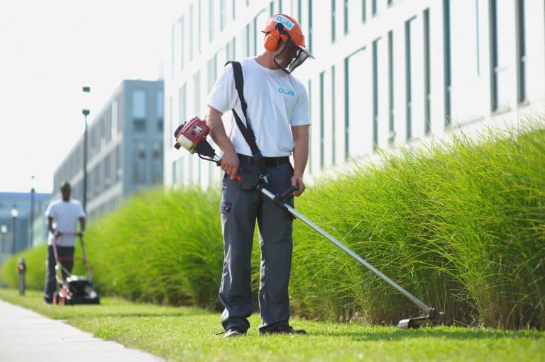 Mitarbeiter des Gebäudeservices Clean Excellence Facility Management mit Helm und Schutzkleidung bei der Grünrasen-Pflege mit Werkzeug.