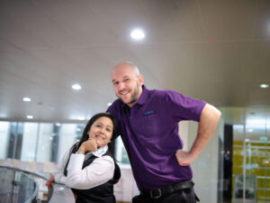 Zwei Mitarbeiter der Clean Excellence Gebäudereinigung (links eine Dame, rechts ein Herr) lachen freundlich in die Kamera.